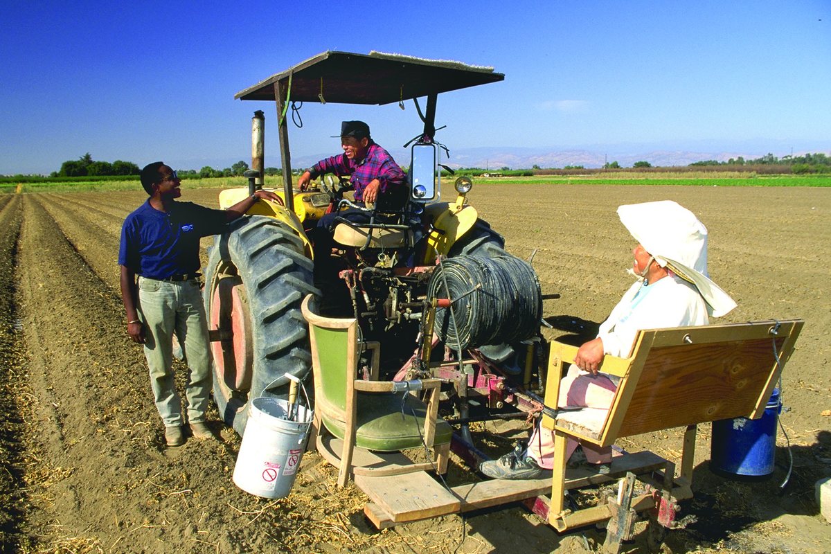 A farm family transplanting a field from a tractor while a USDA conservationist talks with them