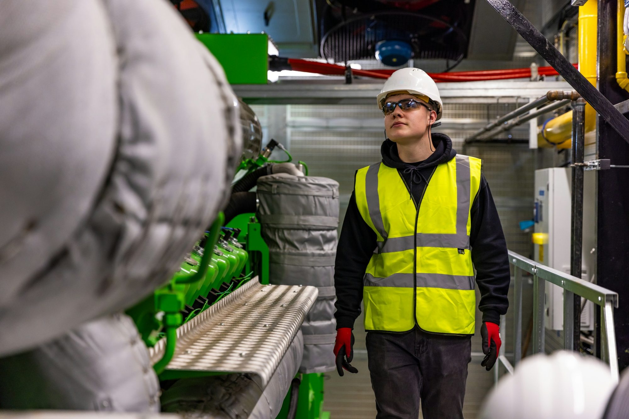 Technician in a hard hat and safety vest inspecting generator engines in an engine hall
